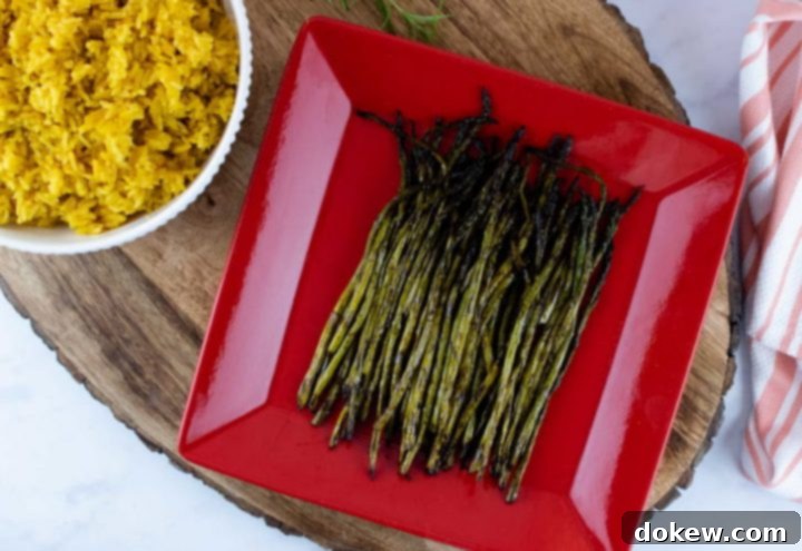 grilled-asparagus-post-min grilled asparagus on a red serving plate placed on a wood serving tray with a bowl of yellow rice and a tea towel to the side