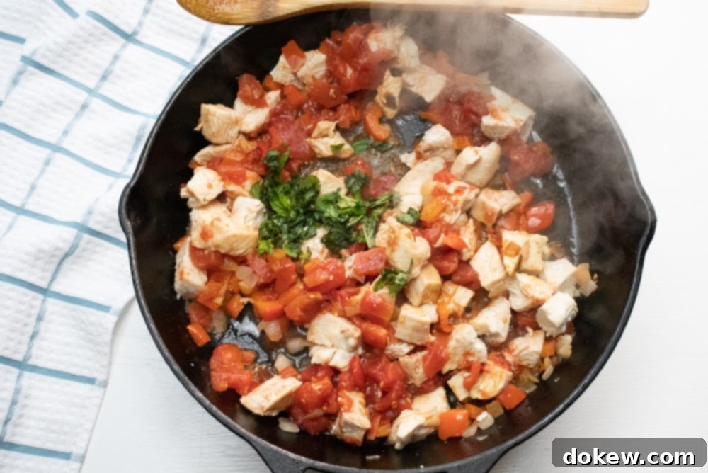 Sautéing Vegetables and Chicken for Mediterranean Pasta Cast iron skillet cooking chopped chicken, diced tomatoes, and fresh basil for Mediterranean pasta