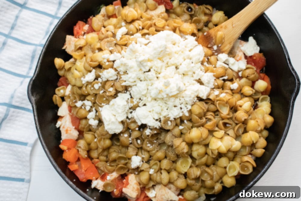 Tossing Mediterranean Pasta with Balsamic and Feta Cast iron skillet with shell pasta, tomatoes, onions, feta cheese, and balsamic vinegar being mixed