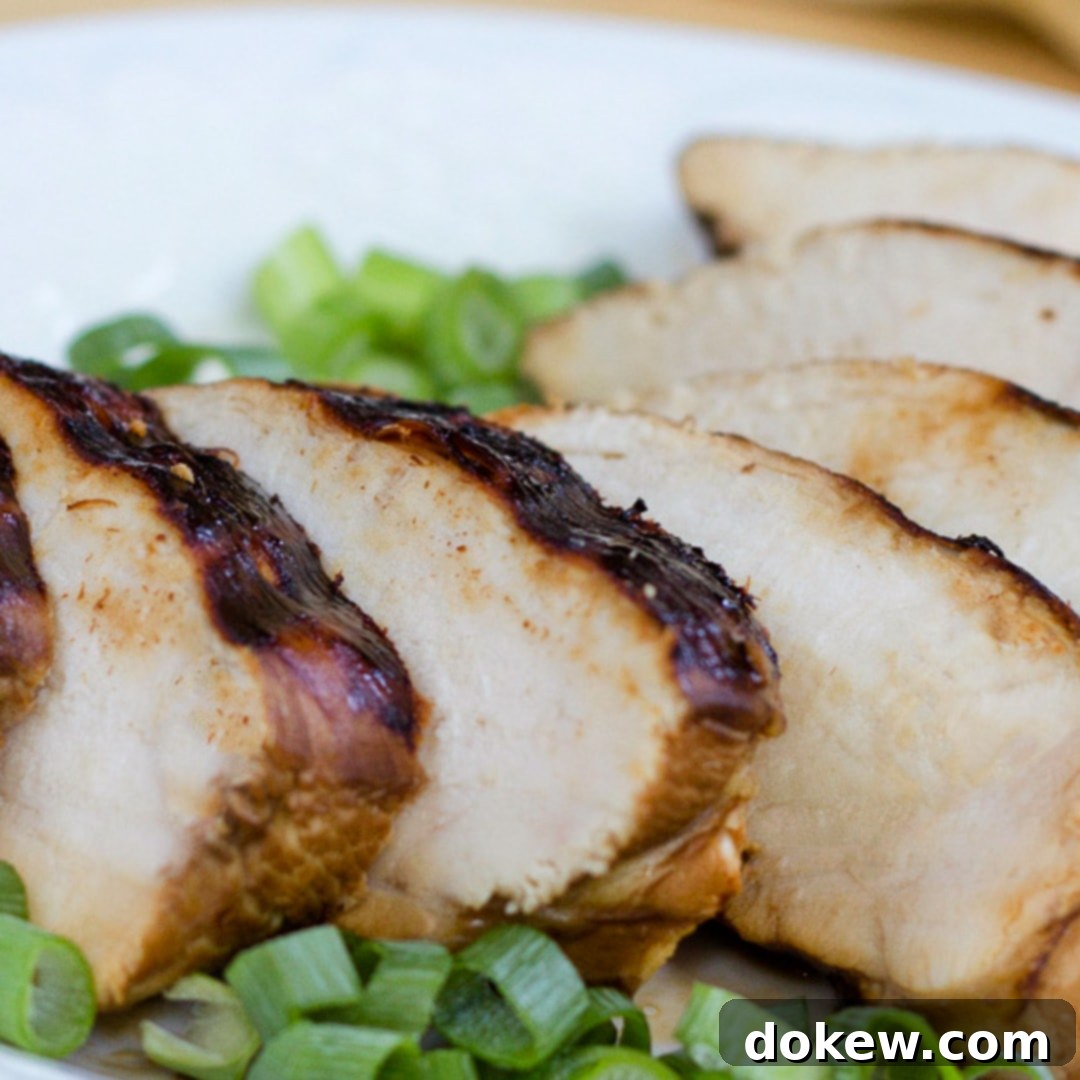 Bulk cooking chicken for the freezer can save hours of prep time Perfectly sliced grilled chicken breast on a pristine white plate, elegantly garnished with freshly chopped green onions, ready for serving or meal prep.