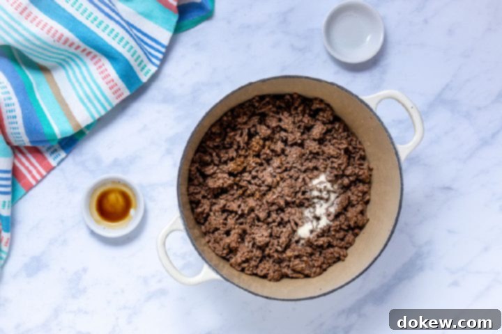 Legendary Terlingua Chili 6 Cooked ground beef simmering in a Dutch oven, infused with Worcestershire sauce and seasoned salt, presenting a rich brown color.