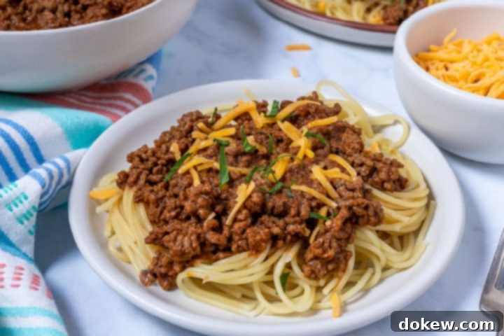 Legendary Terlingua Chili 9 A bowl of Terlingua chili served over a bed of spaghetti, generously garnished with shredded cheddar cheese, showcasing the classic 'chili three-way' style.