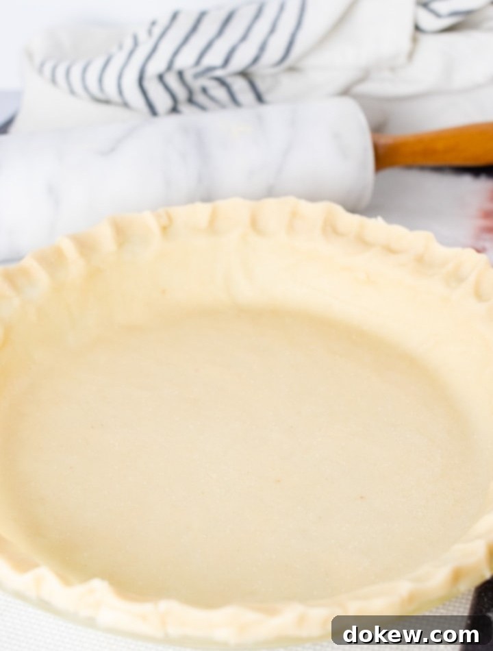 bulk-pie-crust-post-vert-min Unbaked pie crust in a pie pan with a marble rolling pin and flour sack towel in the background