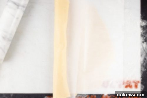 Make-Ahead Buttery Flaky Pie Crust 11 pie crust dough partially rolled up in parchment paper on a rolling mat with a marble rolling pin to the side