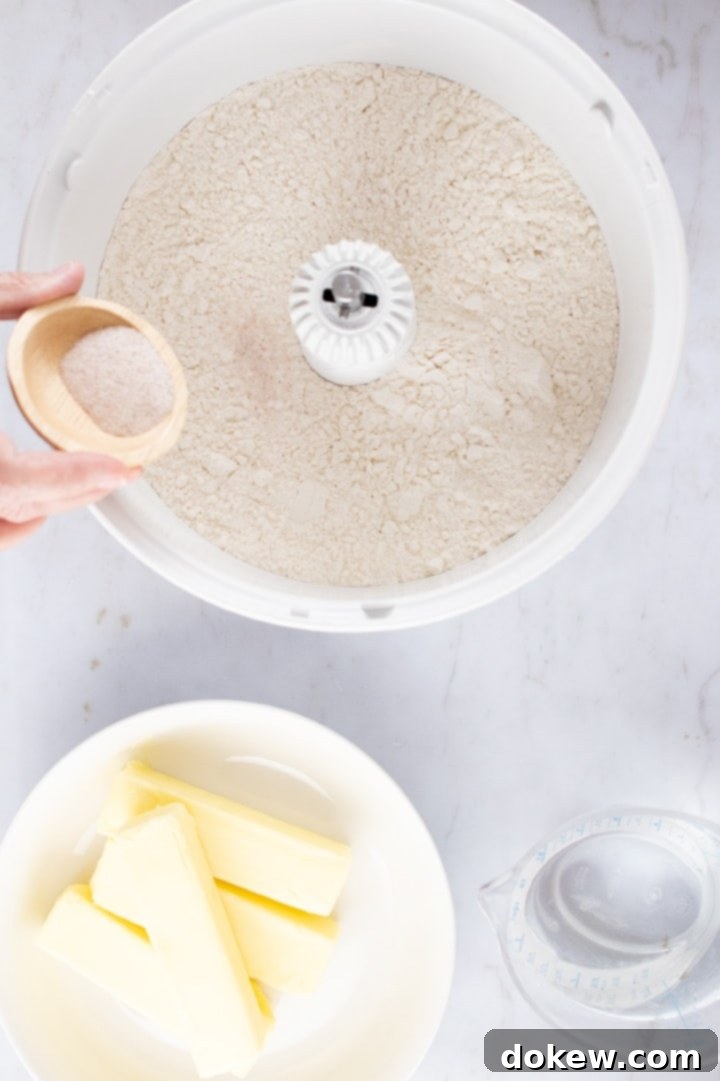 Make-Ahead Buttery Flaky Pie Crust 2 Overhead shot of flour in a mixer with salt being added from a small wooden bowl and containers of butter and water to the side