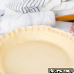 Make-Ahead Buttery Flaky Pie Crust 6 Unbaked pie crust in a pie pan with a marble rolling pin and flour sack towel in the background