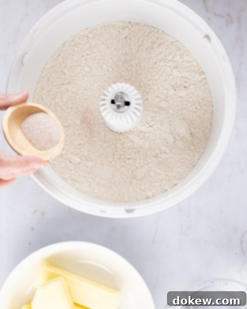 Make-Ahead Buttery Flaky Pie Crust 7 Overhead shot of flour in a mixer with salt being added from a small wooden bowl and containers of butter and water to the side