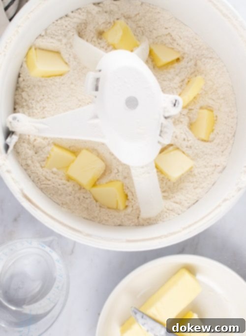 Make-Ahead Buttery Flaky Pie Crust 8 Overhead shot of flour in a mixer with chopped butter added throughout, a bowl with two sticks of butter to the side, and a measuring cup with 1-½ cups water to the side