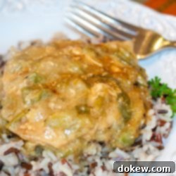 Creamy Green Chili Creole Chicken 2 Chicken with chili cream sauce on a bed of rice on a white plate. There is a fork at the top of the plate.