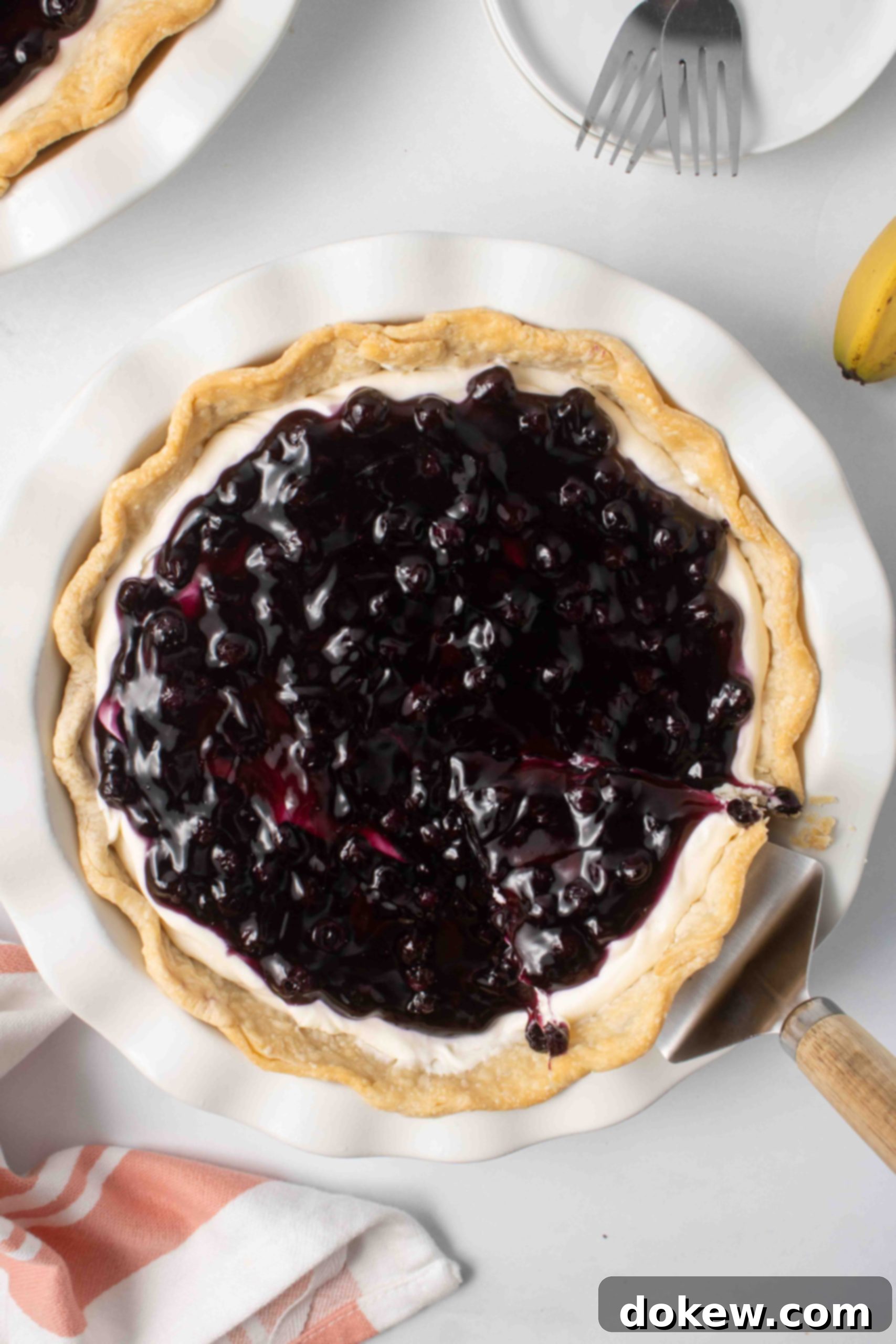 Blueberry Banana Cheesecake Pie 10 Overhead view of a blueberry banana pie with a slice being lifted out.