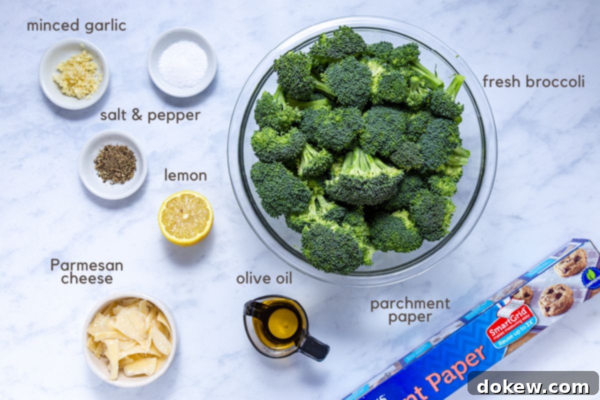 Crispy Garlic Roasted Broccoli 3 A curated display of ingredients for Roasted Garlic Broccoli: a large bowl brimming with vibrant green broccoli florets, small separate bowls holding kosher salt, freshly ground black pepper, minced garlic, and grated Parmesan cheese. A half-cut lemon and a measuring cup with golden extra virgin olive oil complete the setup, with a roll of parchment paper lying beside them.