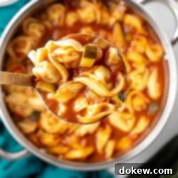 Garden Zucchini Tortellini Pot 7 A ladle lifts a spoonful of Tomato Zucchini Soup with tortellini from a pot, ready to serve.