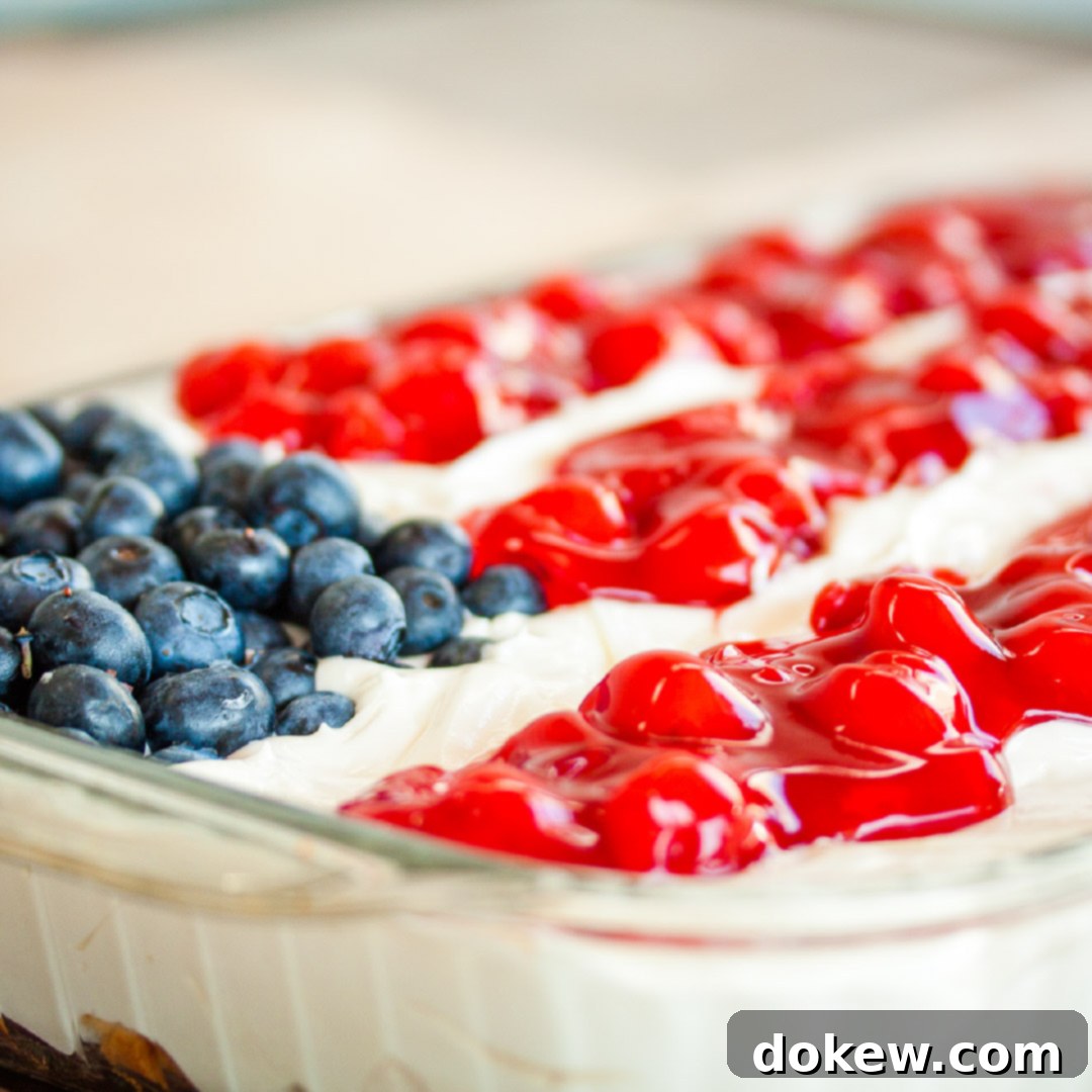 Fluffy white whipped cream mix over crumbled angel food cake topped with blueberies and cherry pie filling in the design of an American flag in a 9x12 glass pan