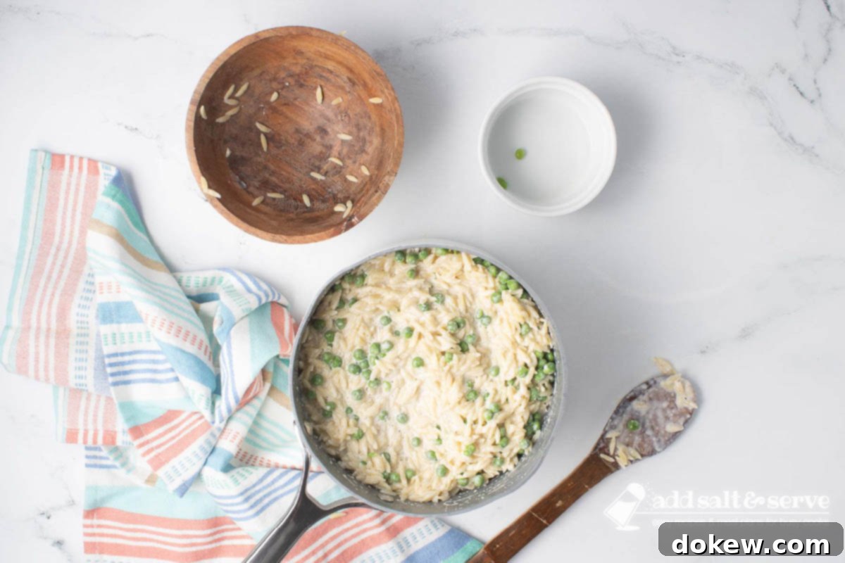 Velvety Orzo Alfredo 8 Cooked orzo and thawed peas being gently mixed into the rich, homemade Alfredo sauce in a large saucepan.