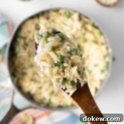 Velvety Orzo Alfredo 9 Serving of Orzo Alfredo with peas on a wooden spoon above the pot.