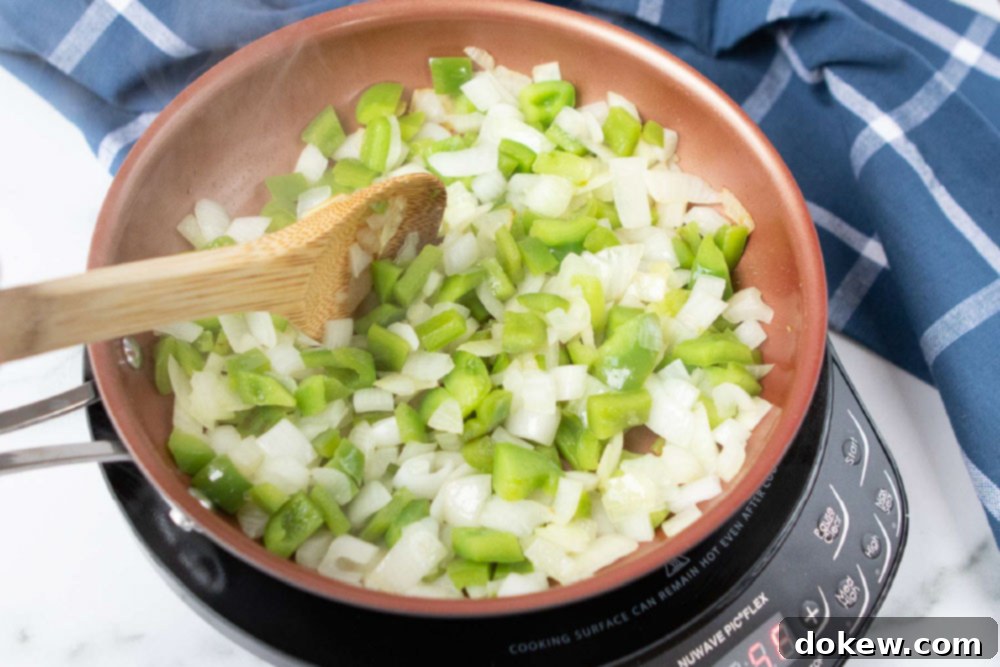Crockpot Albondigas Soup (Mexican Meatball Soup) Chopped onion and green bell pepper in a fry pan being stirred with a wooden spoon