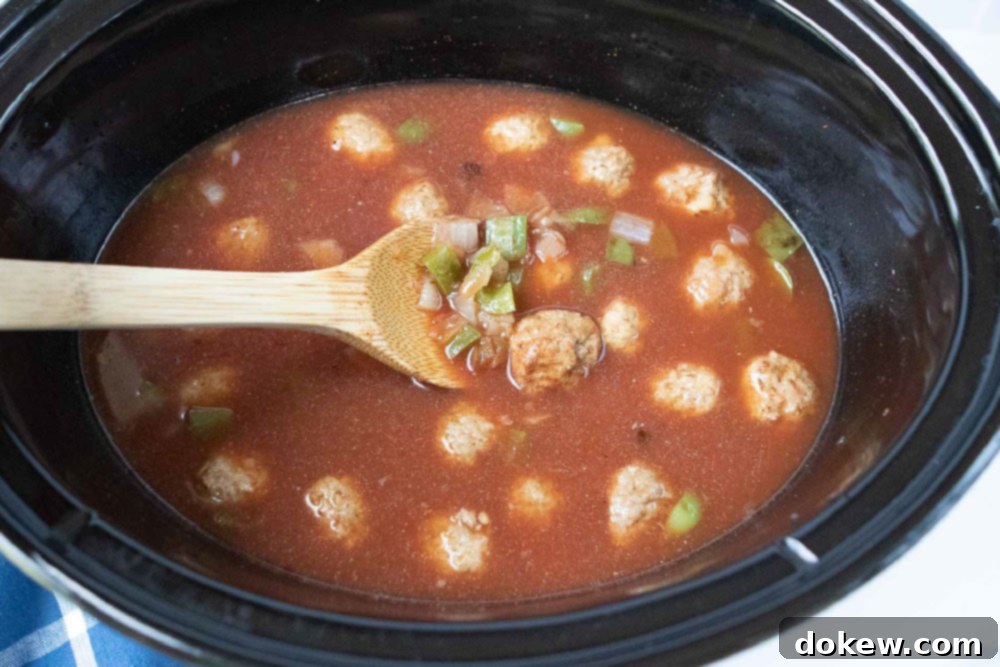 Crockpot Albondigas Soup (Mexican Meatball Soup) Overhead view of meatballs, onions, and bell peppers cooking in a beef and tomato broth in a crockpot