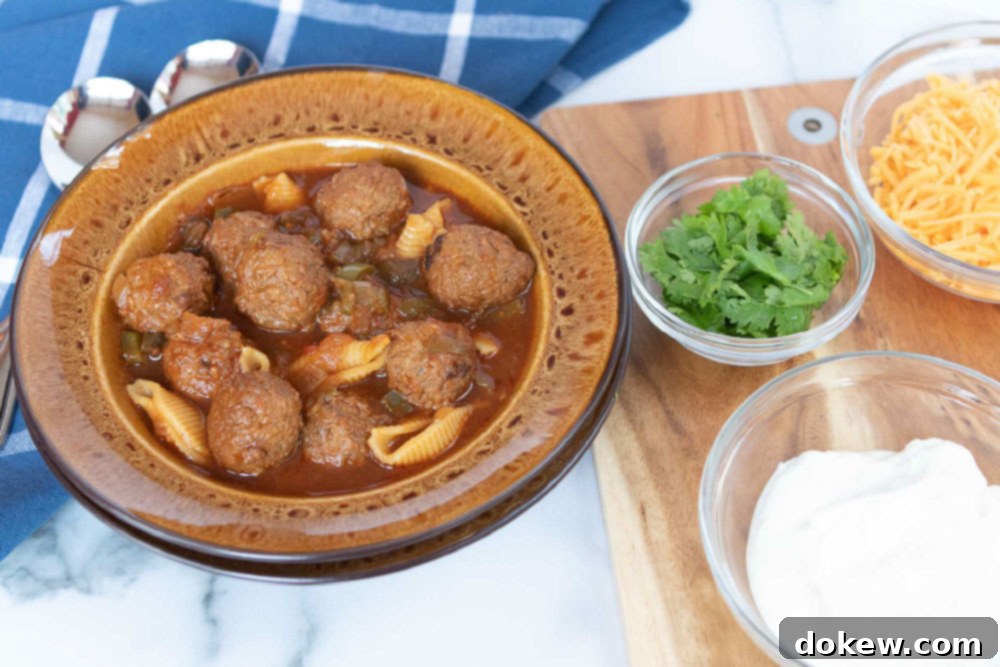 Crockpot Albondigas Soup (Mexican Meatball Soup) Overhead shot of albondigas soup (Mexican meatball soup) in a brown wide-rim bowl with bowls of sour cream, grated cheddar cheese, and fresh cilantro to the side
