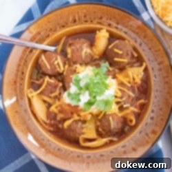 Comforting Slow Cooker Mexican Albondigas Soup 2 Overhead shot of albondigas soup (Mexican meatball soup) in a brown wide-rim bowl garnished with sour cream, grated cheddar cheese, and fresh cilantro
