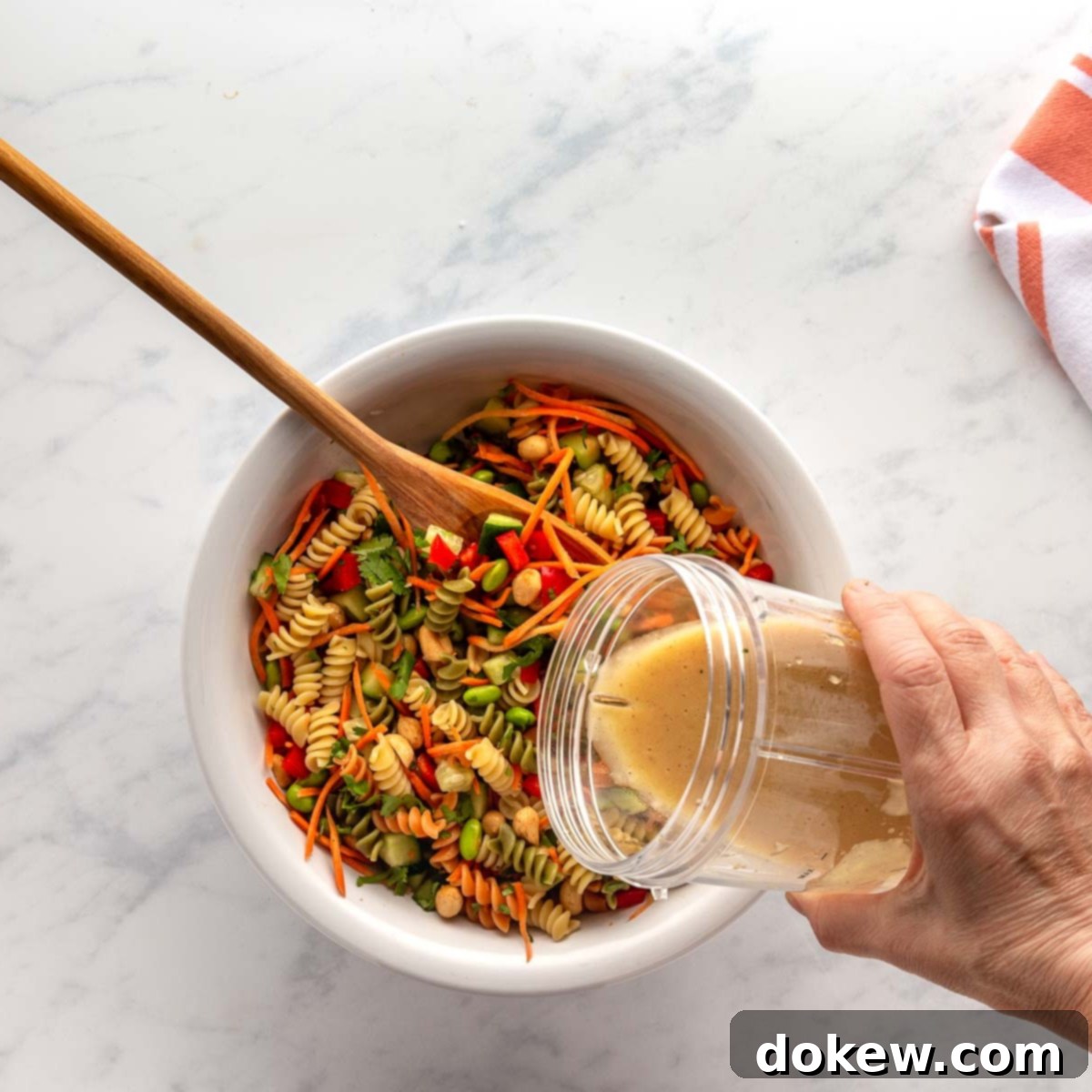 Pouring sesame ginger dressing over Thai pasta Salad, showcasing the dressing's smooth texture and appetizing color.