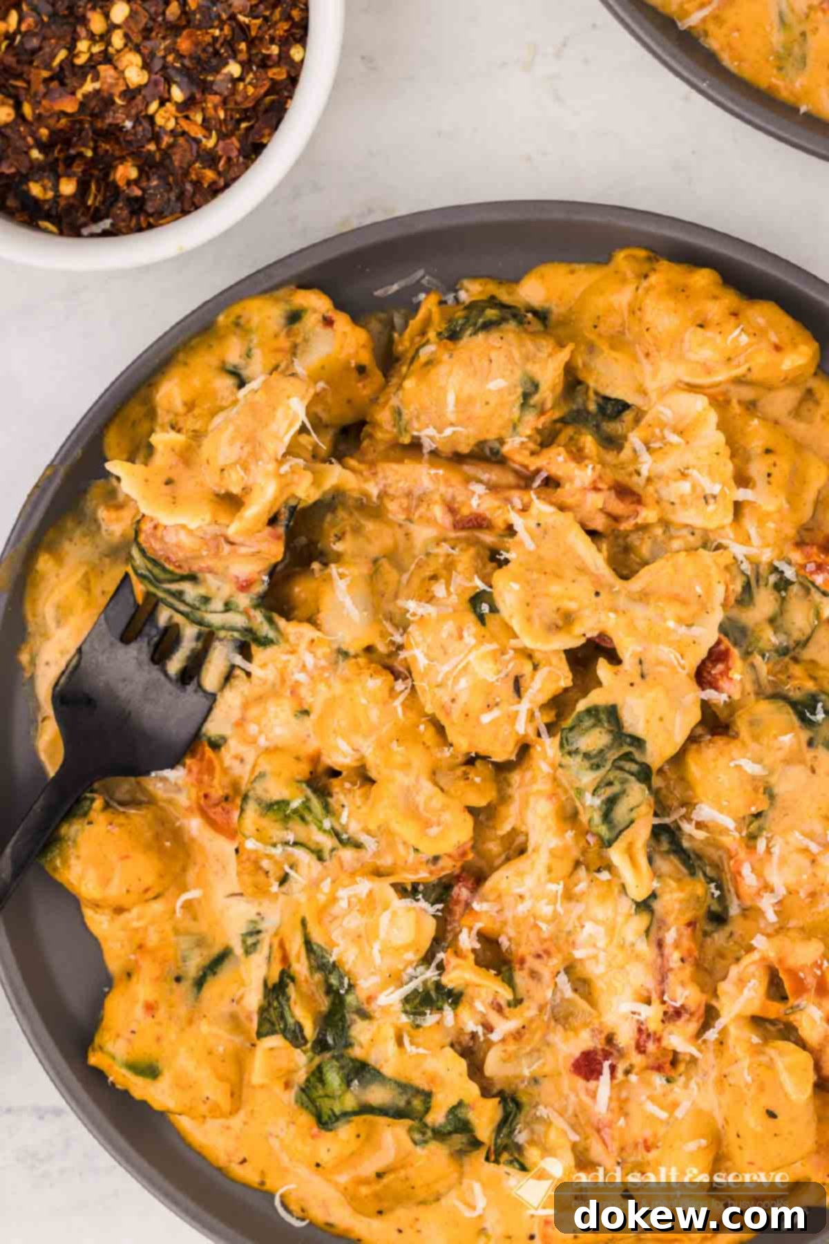 Tuscan Sunset Chicken 6 A delectable serving of creamy Tuscan chicken with sun-dried tomatoes, spinach, and mini farfalle pasta, elegantly plated with a forkful resting on the side, highlighting the dish's rich cream sauce and tender ingredients.