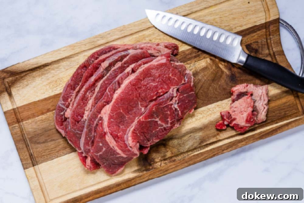 Easy Crockpot French Dip Tender Beef and Flavorful Au Jus 4 Slices of chuck roast on a cutting board with excess fat meticulously trimmed off, ready for the slow cooker.