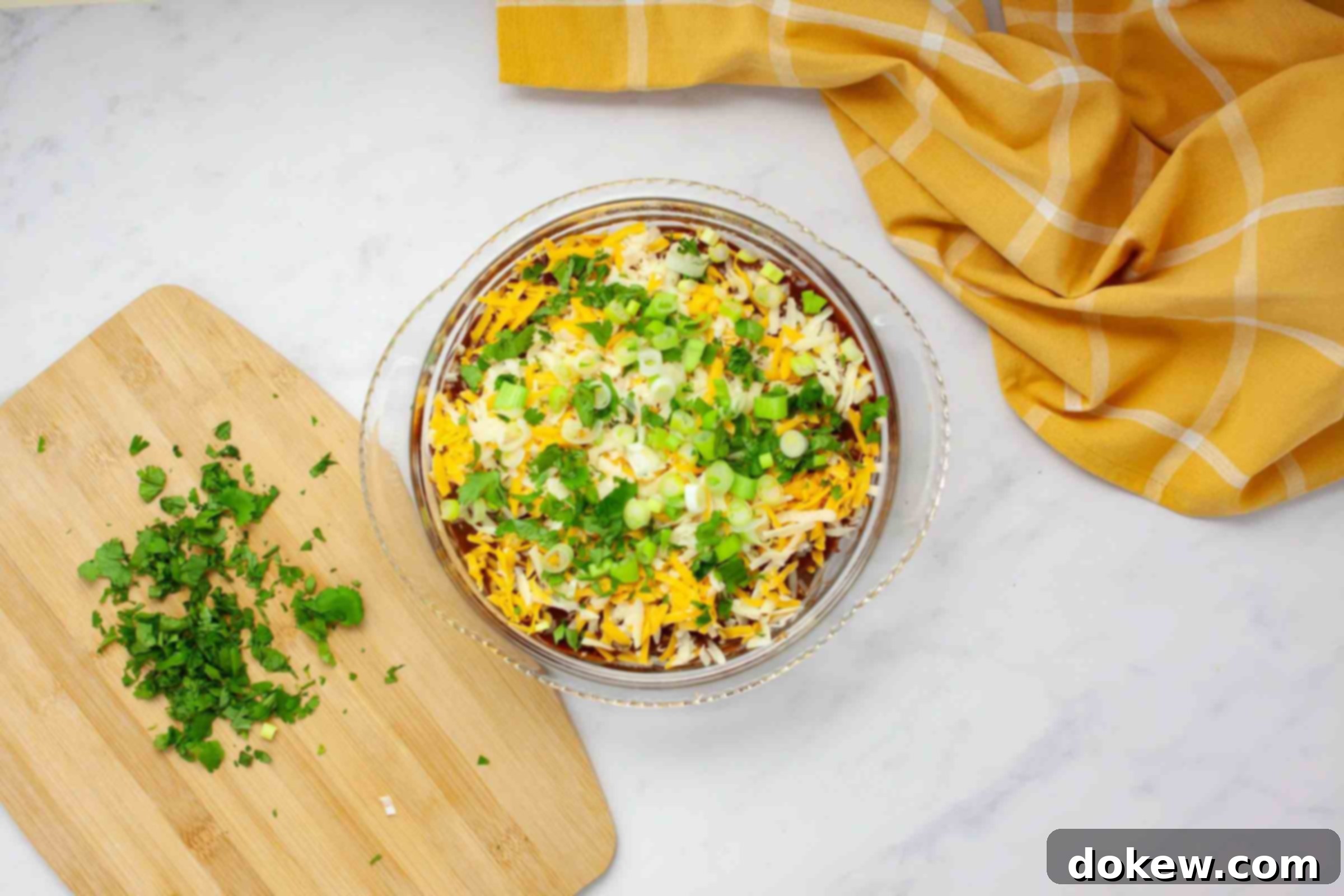 Simple Stacked Chicken Enchilada Casserole 7 An overhead view of a pie dish filled with a layered chicken enchilada bake, beautifully topped with green onions and cilantro, ready for baking. The layers of rich enchilada sauce, tender chicken, and melty cheese are visible beneath the final garnish.