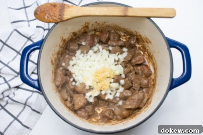 Beef and Guinness Stew Beef stew in a pot with chopped raw onions and garlic added