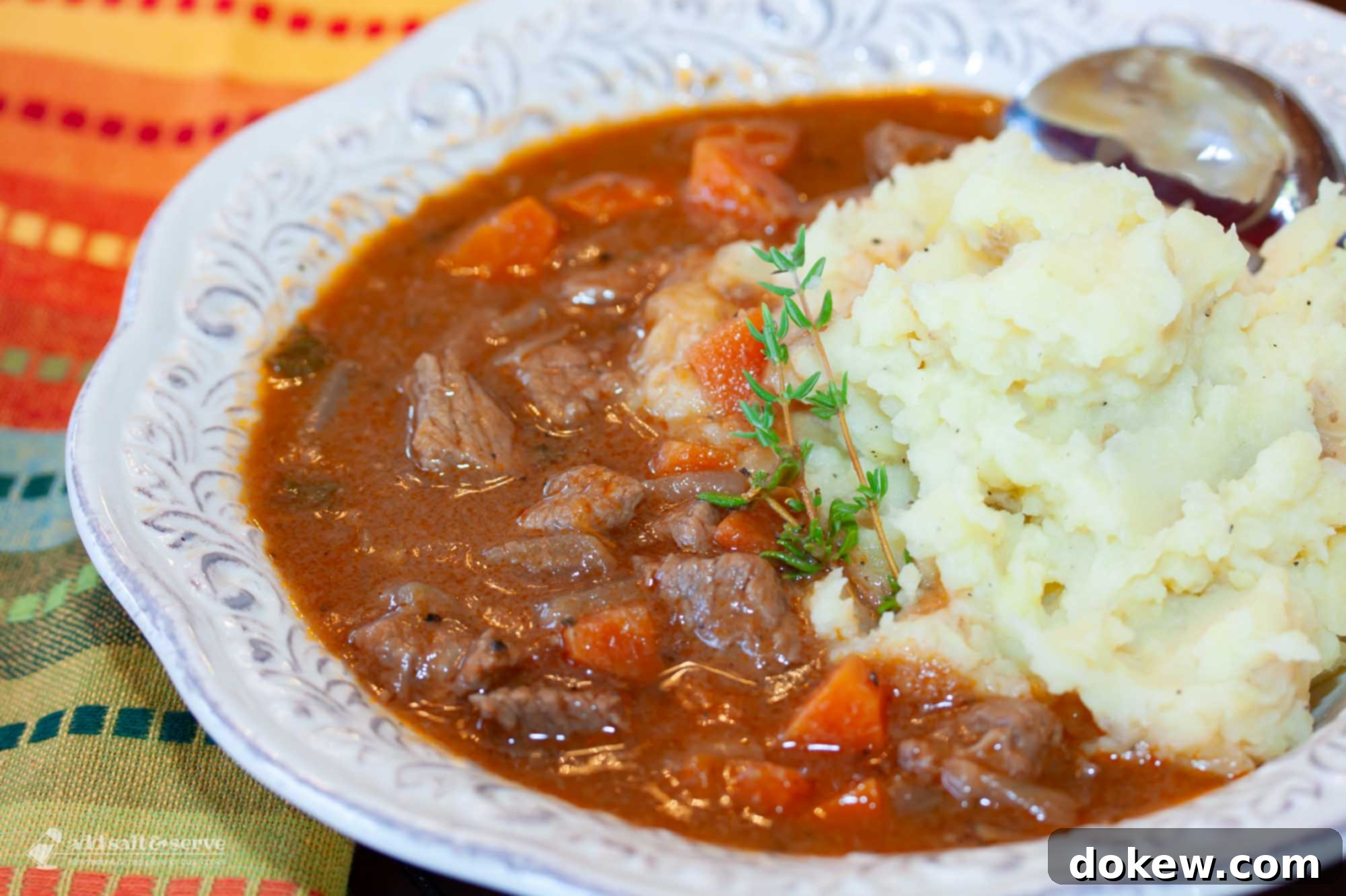 Your Perfect Guinness Beef Stew 2 White bowl with beef stew with carrots served over mashed potatoes garnished with a sprig of thyme.