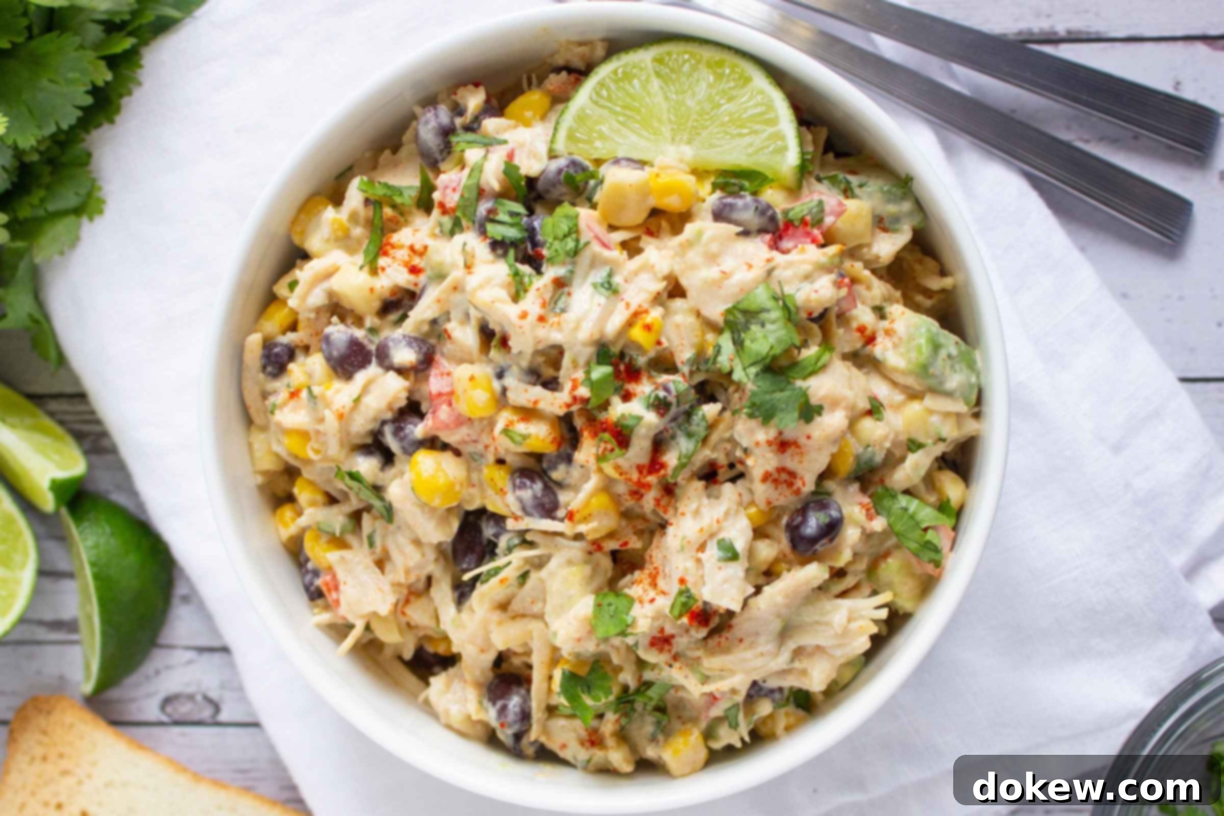 Lime-Kissed Southwest Chicken and Black Bean Salad 2 Bowl of chicken salad with corn, black beans, avocado, and red bell pepper in a creamy dressing garnished with a lime wedge and sprinkled with paprika.