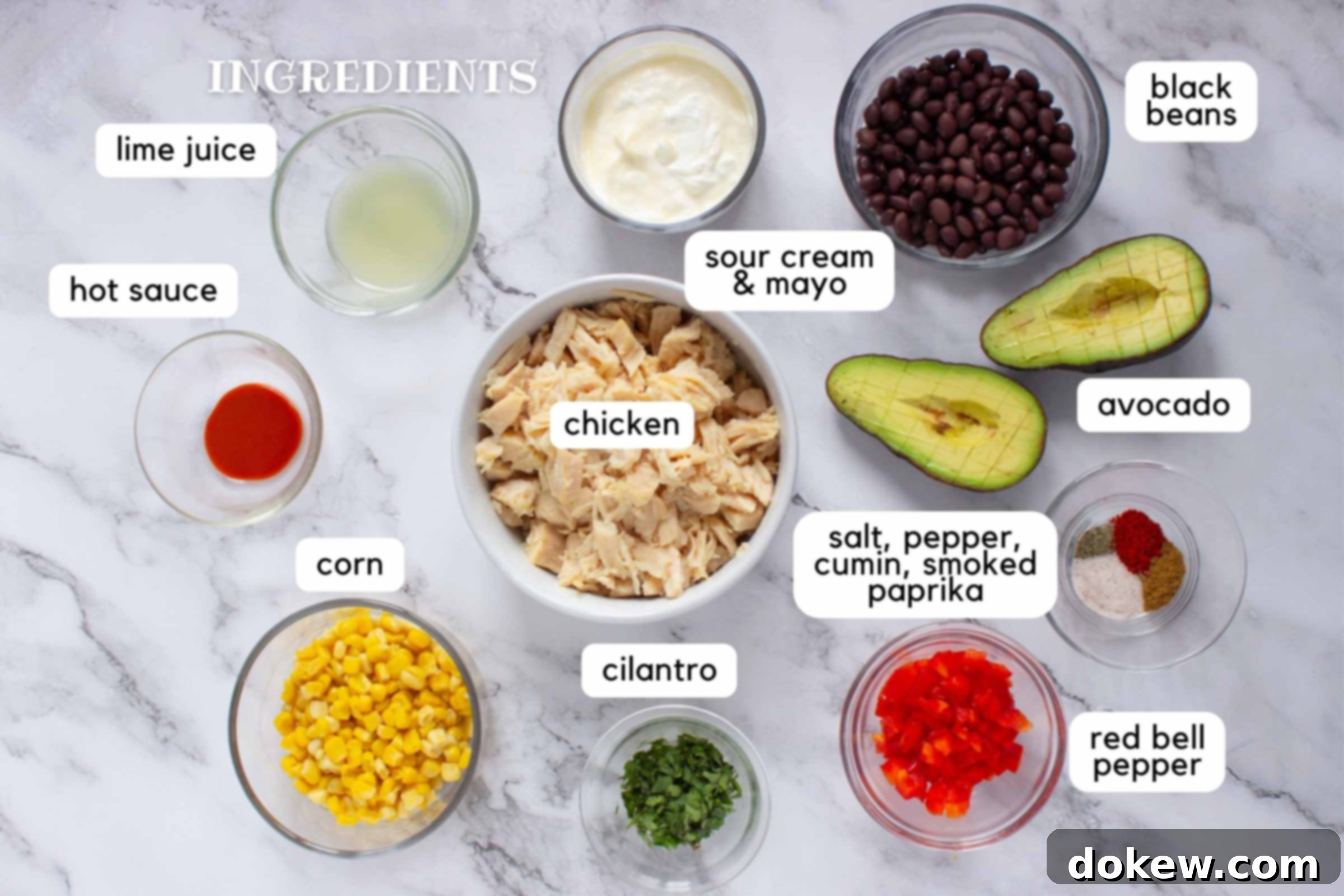 Lime-Kissed Southwest Chicken and Black Bean Salad 3 Labeled ingredients on a counter: Chicken, corn, cilantro, salt, pepper, cumin, smoked paprika, red bell pepper, avocado, black beans, sour cream & mayo, lime juice, and hot sauce.