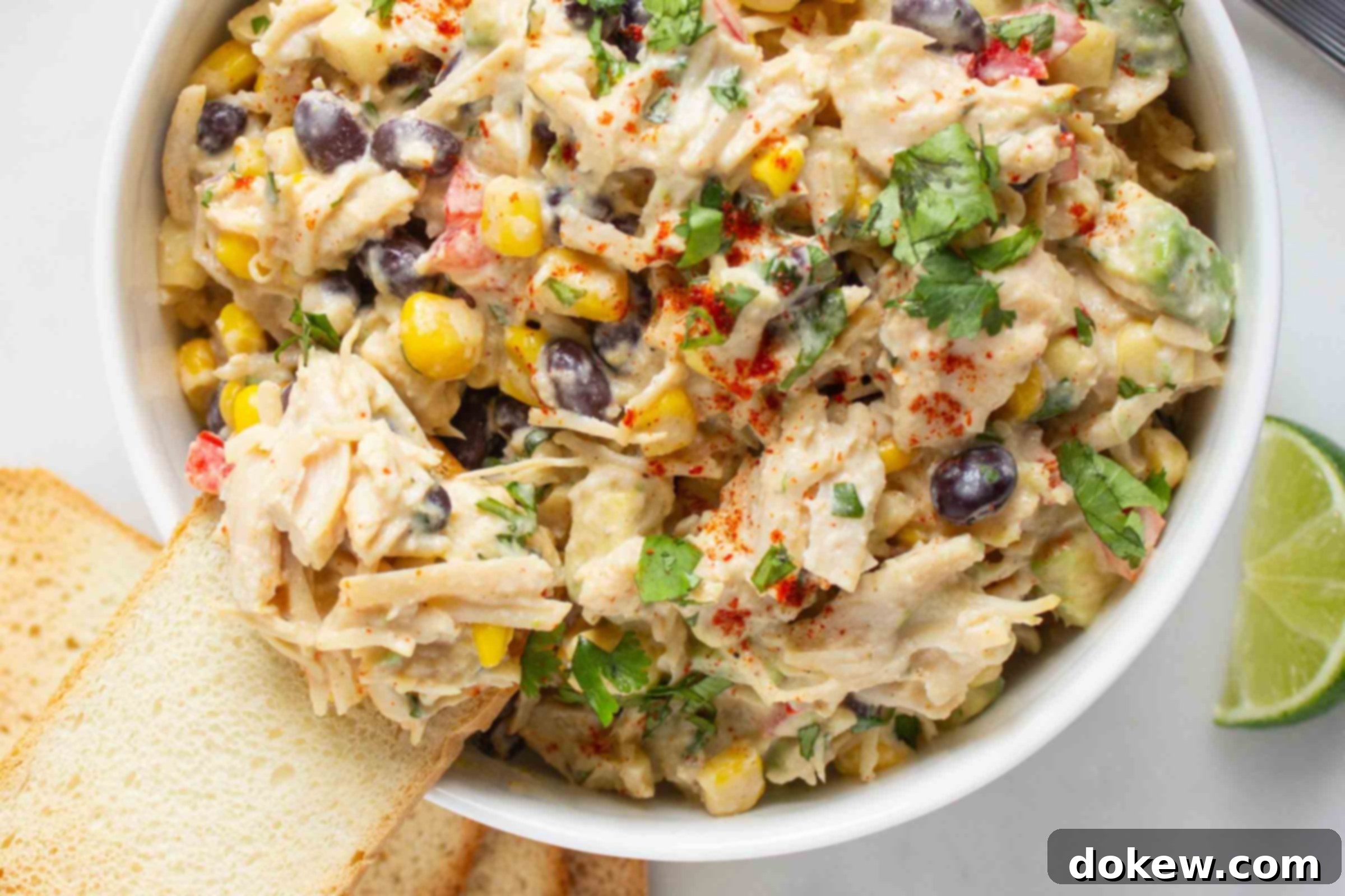 Lime-Kissed Southwest Chicken and Black Bean Salad 5 Bowl of chicken salad with corn, black beans, avocado, and red bell pepper in a creamy dressing sprinkled with paprika beside crostini and a lime wedge.