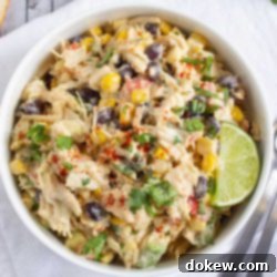Lime-Kissed Southwest Chicken and Black Bean Salad 7 Bowl of chicken salad with corn, black beans, avocado, and red bell pepper in a creamy dressing garnished with a lime wedge and sprinkled with paprika.