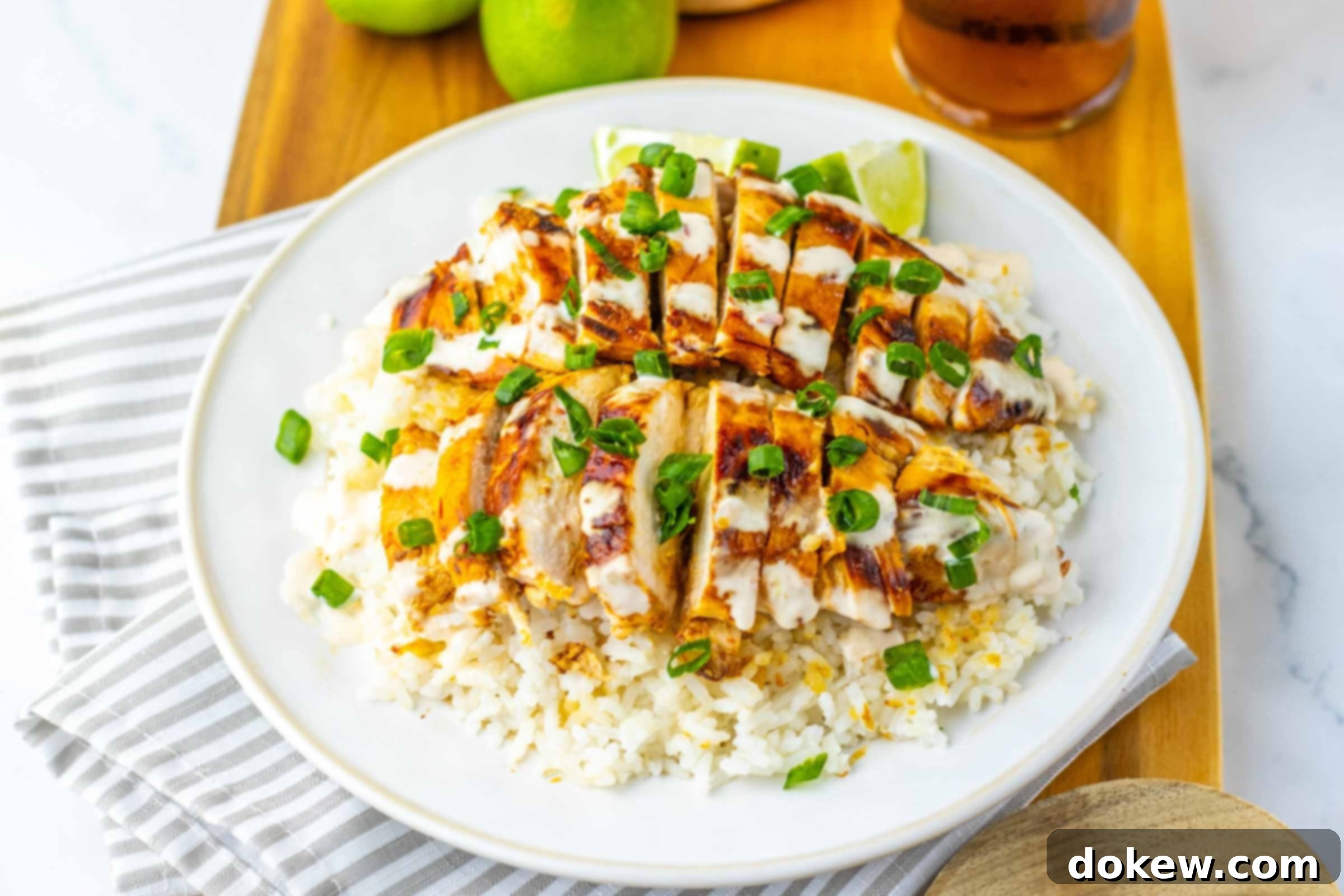 Chicken breast over rice drizzled with white sauce and garnished with green onions beside a glass of iced tea and two limes.
