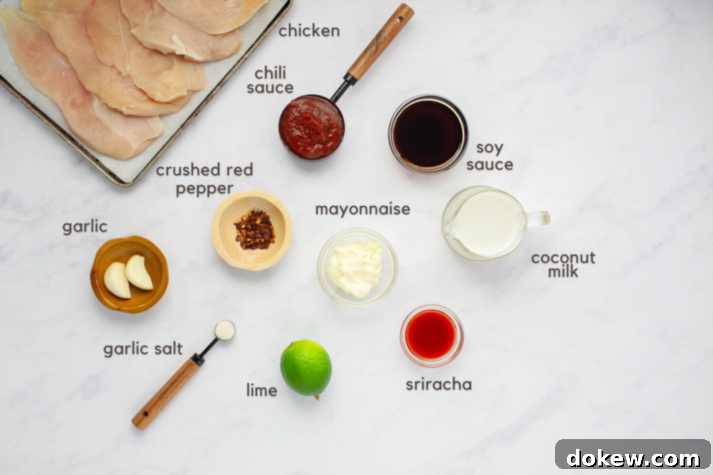 Tropical Chili Lime Chicken with Coconut Lime Sauce 3 Labeled ingredients on a counter: boneless, skinless chicken breasts, chili sauce, soy sauce, crushed red pepper, garlic cloves, garlic salt, lime, mayonnaise, sriracha, and coconut milk.