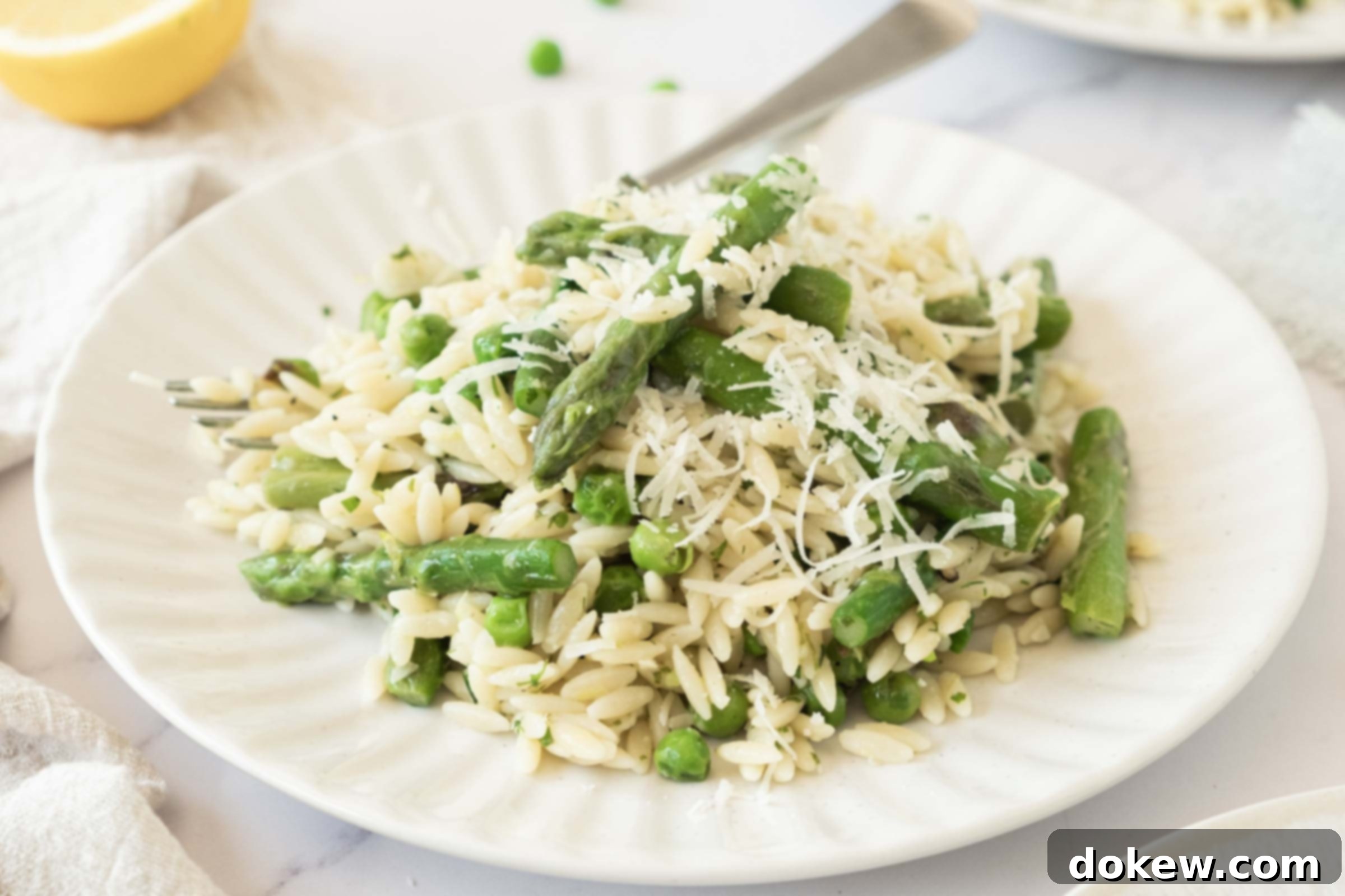 Spring Lemon Orzo with Asparagus, Peas, and Parmesan 2 Plate of orzo with peas and asparagus garnished with grated Parmesan cheese. A close-up view of the vibrant, fresh pasta dish.