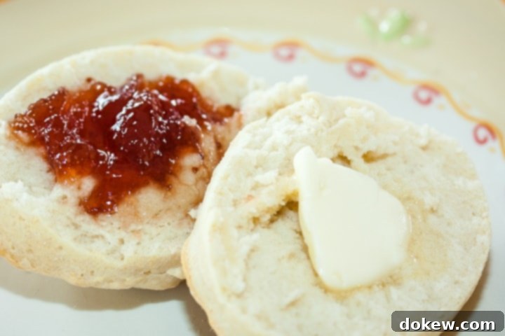homemade-buttermilk-biscuits-post-horiz-min Biscuit cut in half with butter on one half and fruit preserves on the other half on a yellow and white plate