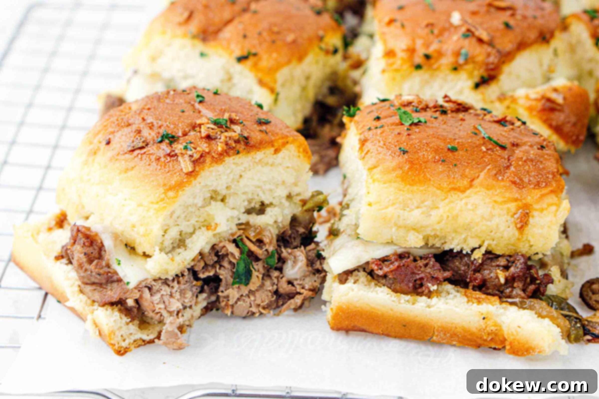 Classic Philly Cheesesteak Sliders 2 Freshly baked Philly cheesesteak sliders on parchment paper, ready to be served.