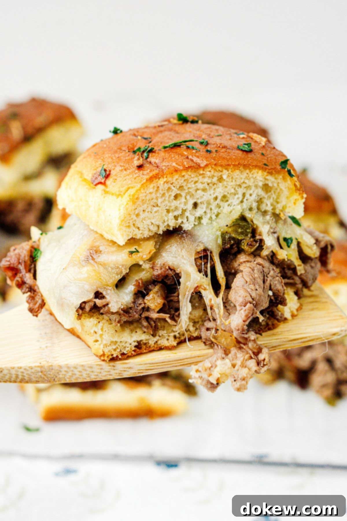 Classic Philly Cheesesteak Sliders 8 A single Philly cheesesteak slider on a wooden spatula raised to the camera, showcasing the melted cheese and filling.