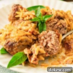 Hearty Tuscan Meatballs with Orzo 8 A plate of meatballs in a creamy red sauce with orzo with a meatball cut open on a fork.
