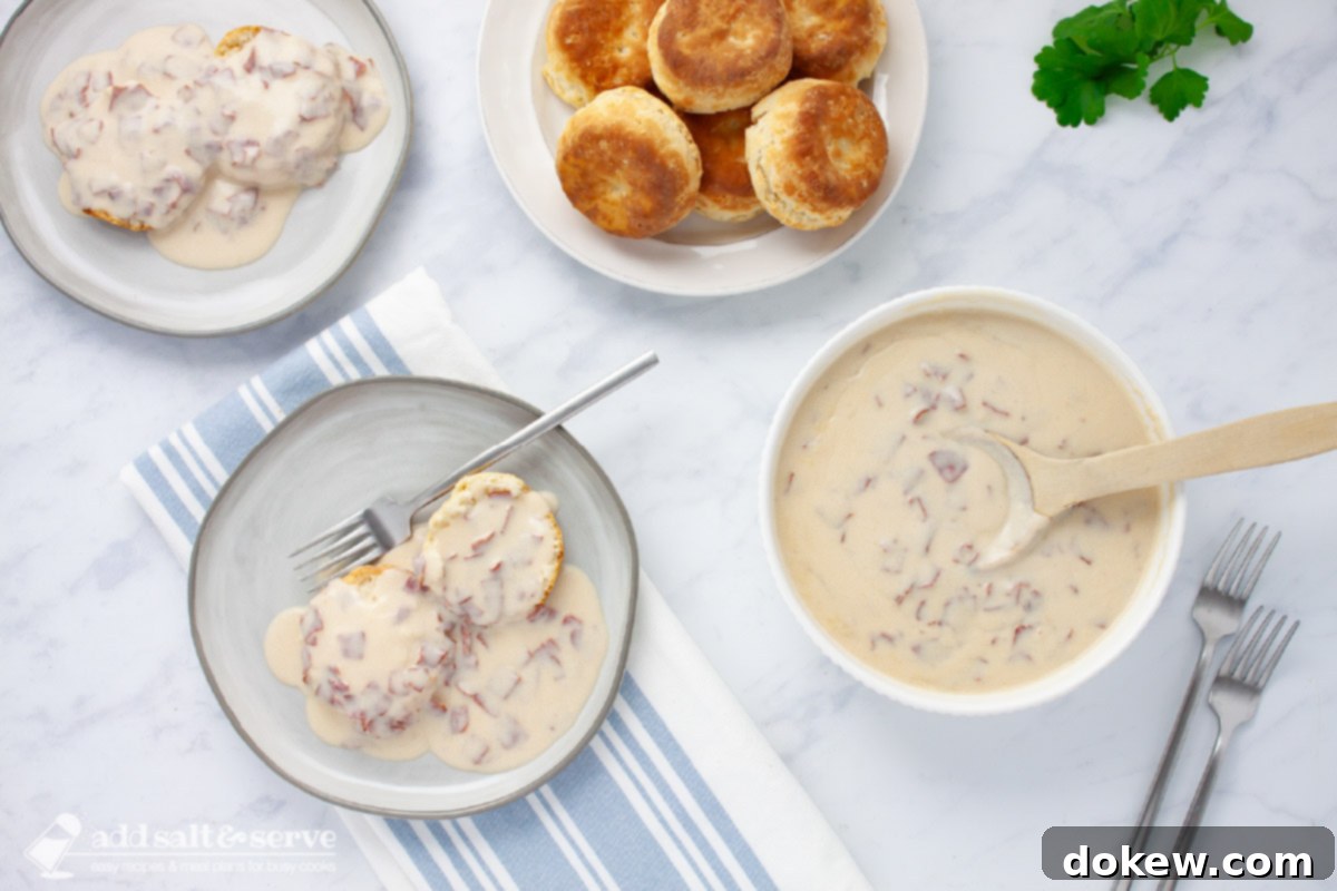 Hearty Chipped Beef Gravy 2 Two plates of creamy chipped beef gravy over two biscuit halves beside a bowl of the gravy with a wooden spoon, evoking a sense of nostalgic comfort.