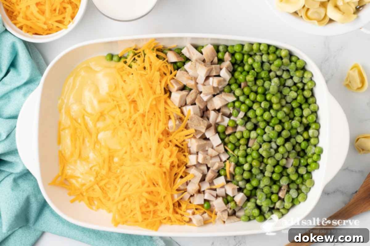 Golden Turkey Tortellini Bake 5 A casserole dish containing condensed cream of chicken soup, shredded sharp cheddar cheese, chopped leftover turkey, and frozen peas, ready to be mixed together.