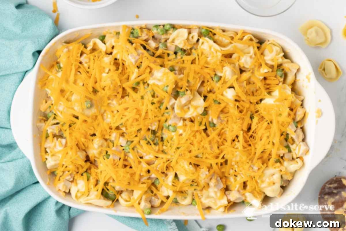 Golden Turkey Tortellini Bake 7 The unbaked casserole, with tortellini, turkey, and peas in a creamy sauce, topped with a generous layer of shredded cheese, ready for the oven.
