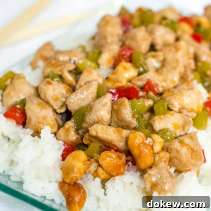 Kung Pao Chicken Diced chicken and diced red and green bell peppers on a bed of rice on a transparent square glass plate.