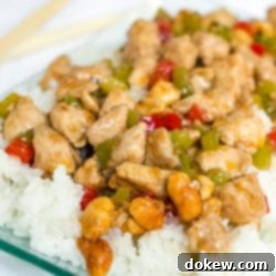 Kung Pao Chicken 2 Diced chicken and diced red and green bell peppers on a bed of rice on a transparent square glass plate.