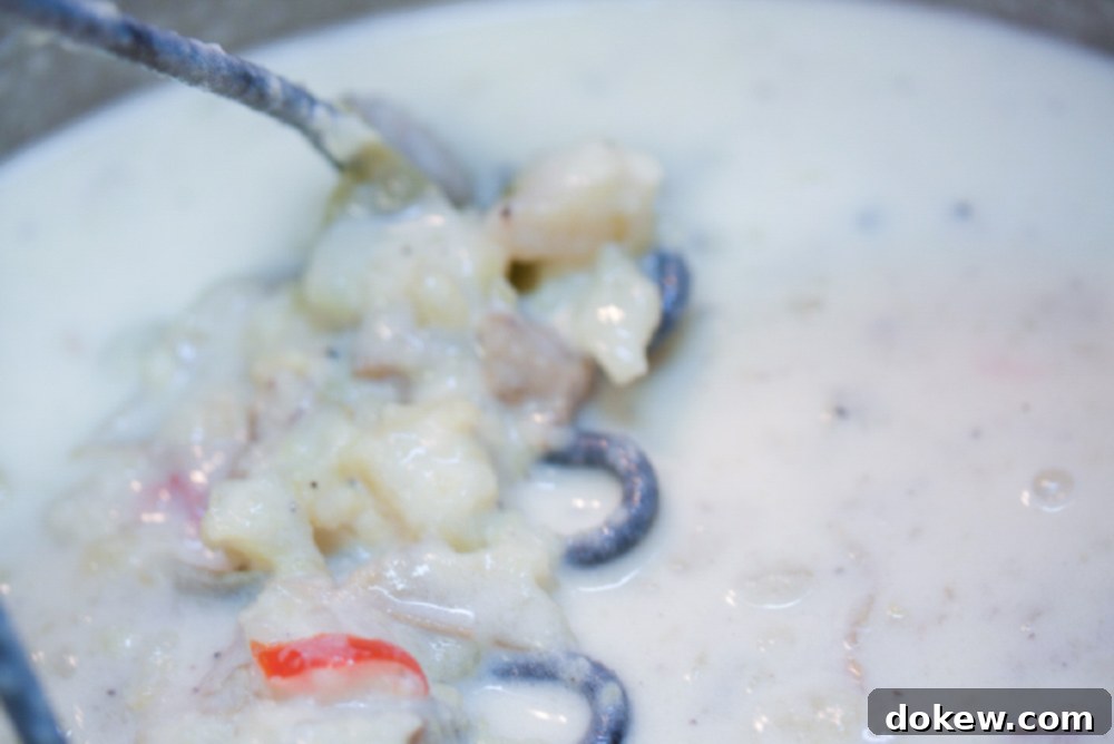 Loaded Baked Potato Soup 5 A potato masher in a bowl of creamy baked potato soup, illustrating the mashing step.