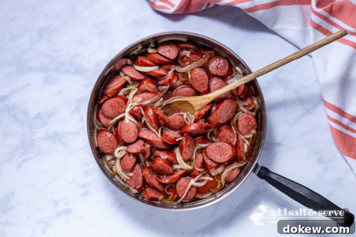 Caramelized Brown Sugar Kielbasa Skillet 6 Skillet with cooked Brown Sugar Kielbasa with a wooden spoon.