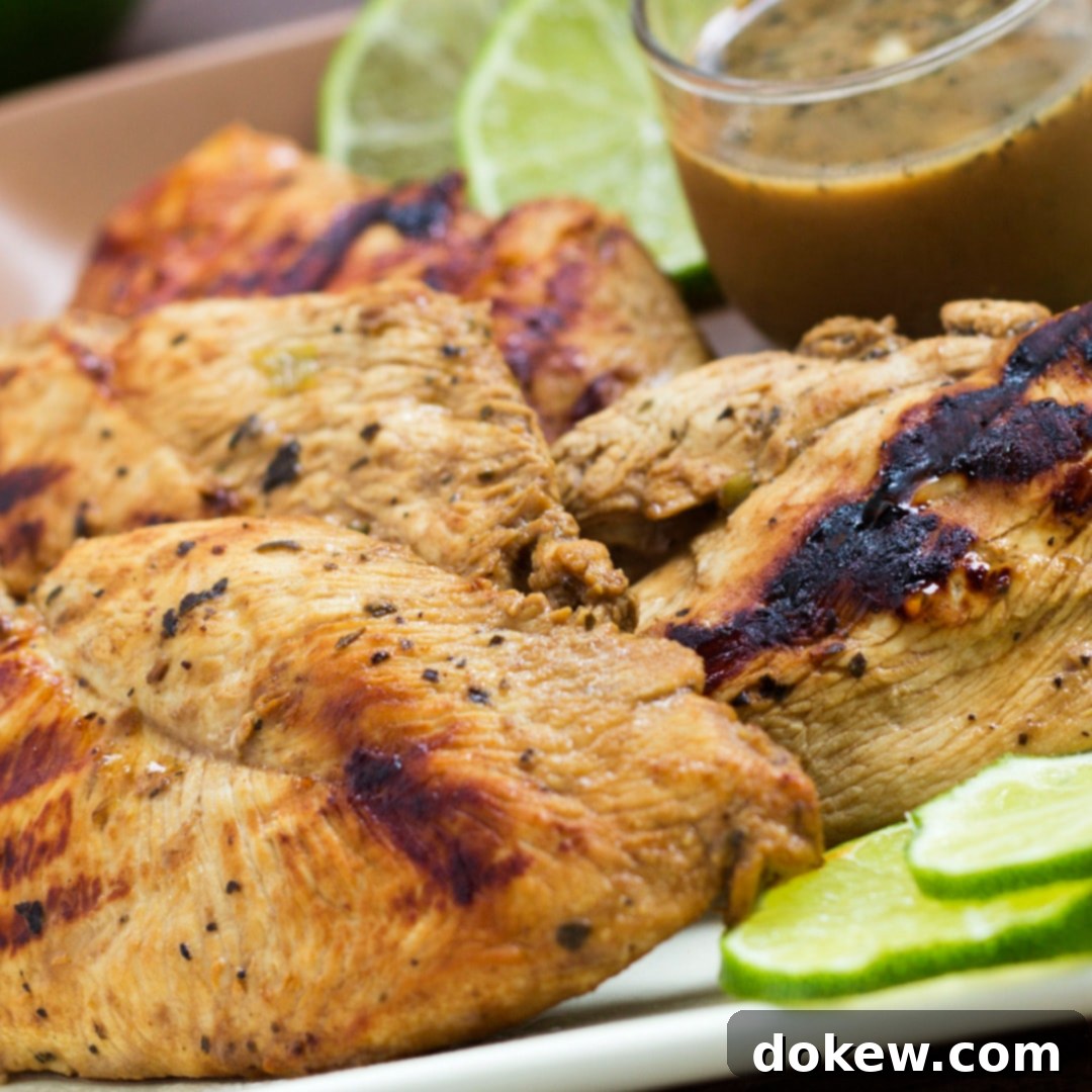 Zesty Basil Lime Chicken 2 Grilled chicken on a square plate, garnished with lime slices. A small clear glass cup of Dijon basil lime dipping sauce is on the plate.