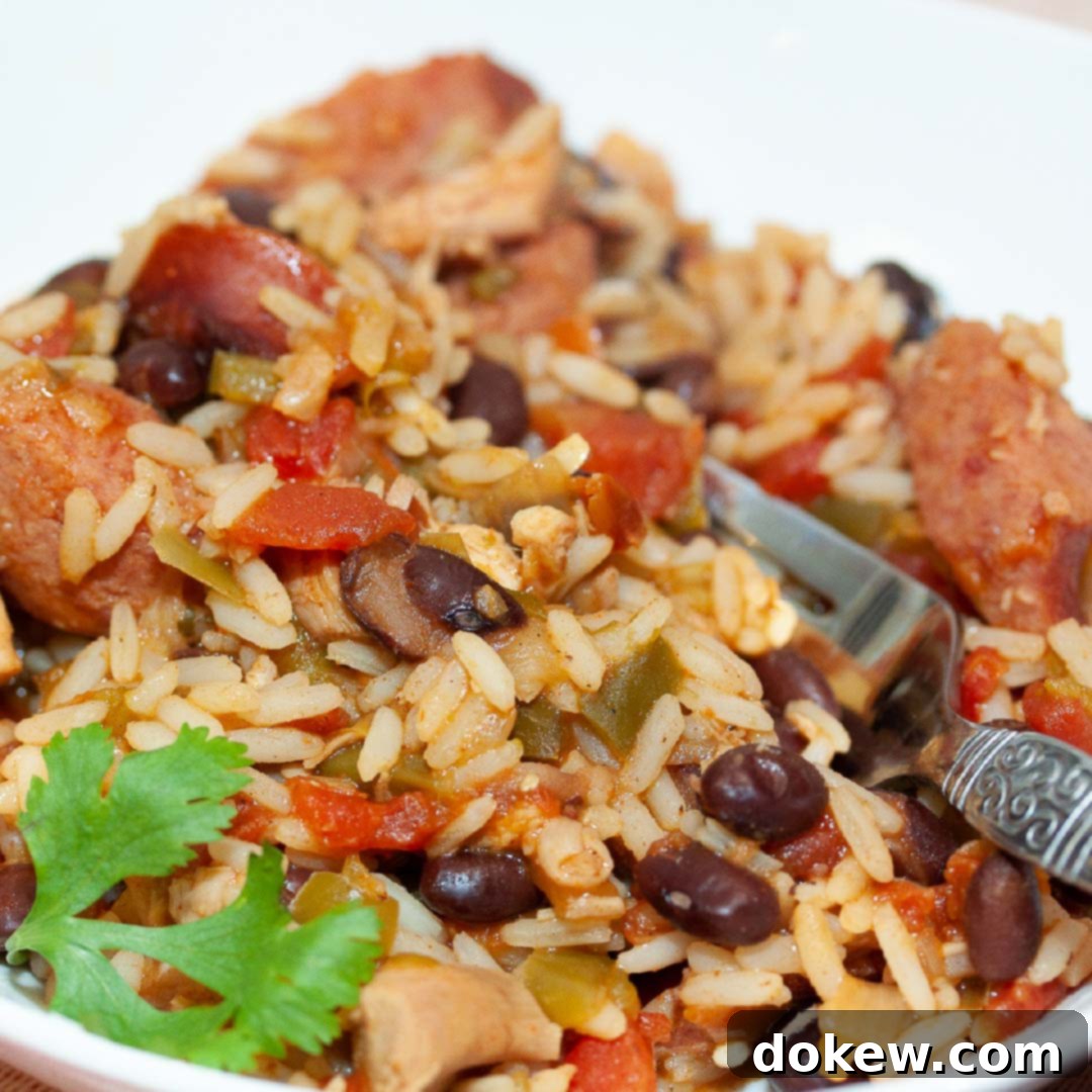 White bowl and fork with rice, black beans, sausage, tomatoes, and green chilies