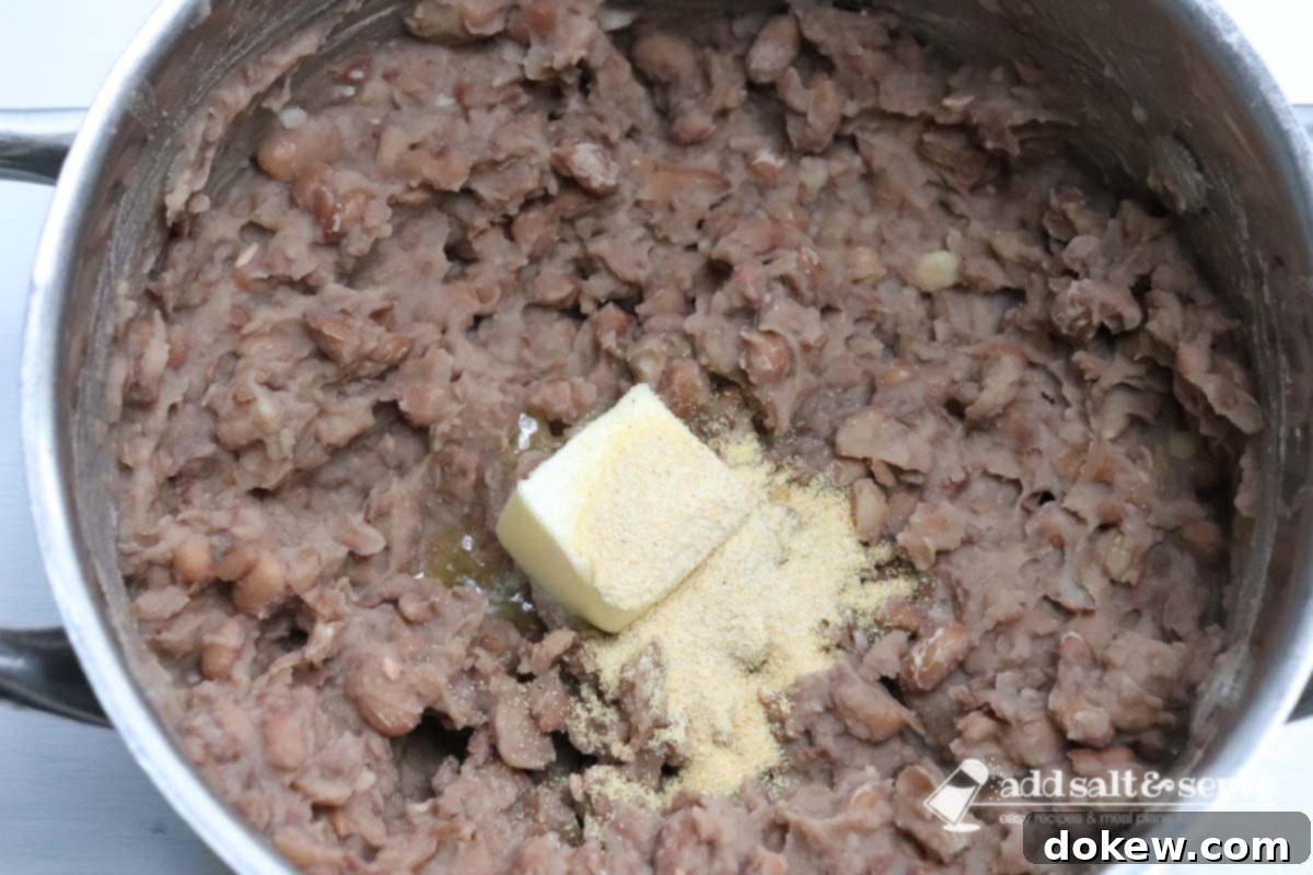 Cooked pinto beans in a large pot with a chunk of butter and adobo seasoning before being mixed in.
